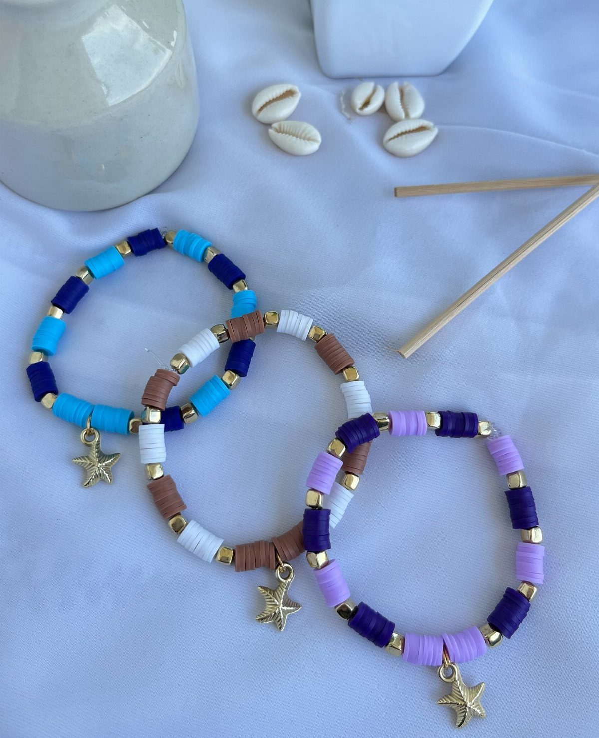 Three colorful clay bead bracelets with gold star charms on white fabric.