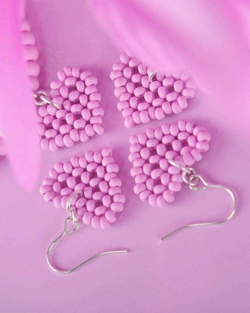 Four light purple beaded heart earrings with silver hooks on a purple background