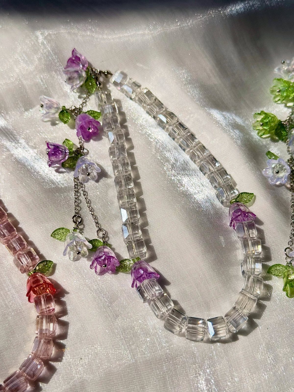 Beaded necklaces with clear and pink crystals and small purple flower accents.