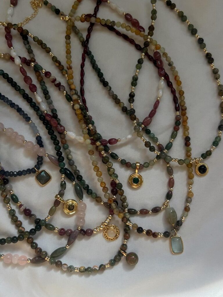 Beaded necklaces in earthy colors with gold pendants on a white fabric background