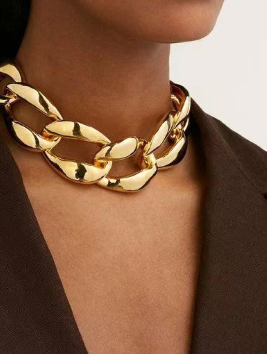 Chunky gold chain link necklace worn by a person in a brown blazer.