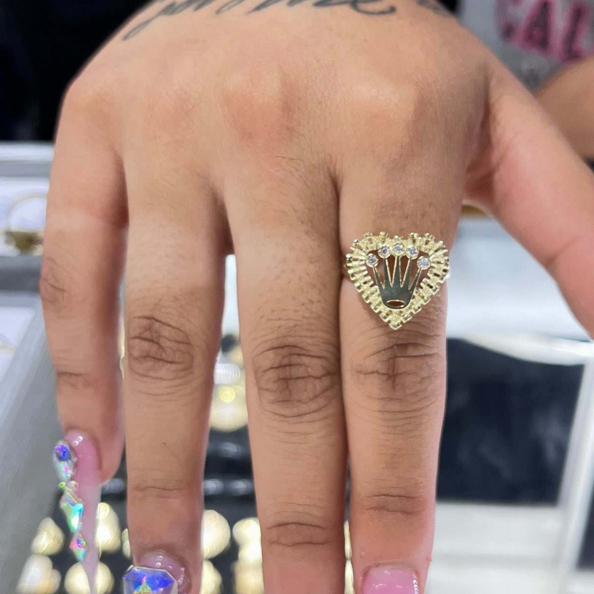 Gold heart-shaped ring with crystals worn on a finger with decorated nails