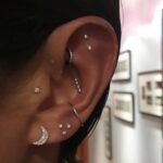 Ear with multiple silver and diamond piercings including a crescent moon stud.