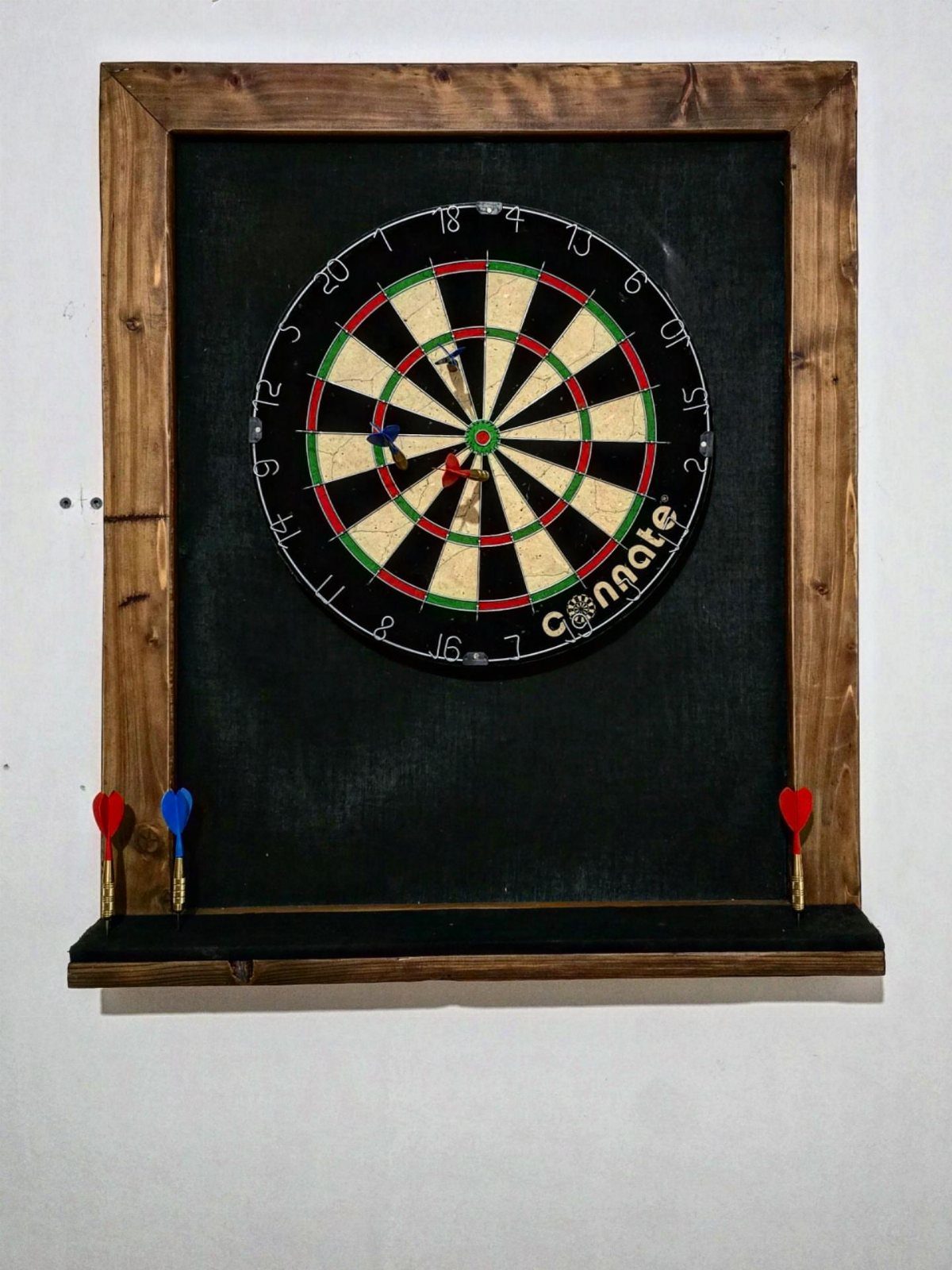 Dartboard mounted on a black backboard with a wooden frame and ledge.