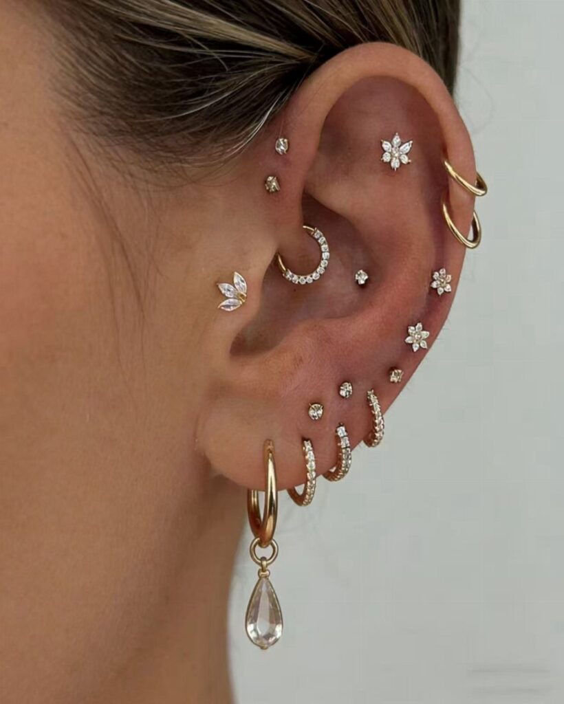 Ear with multiple gold piercings featuring a mix of studs and hoop earrings.