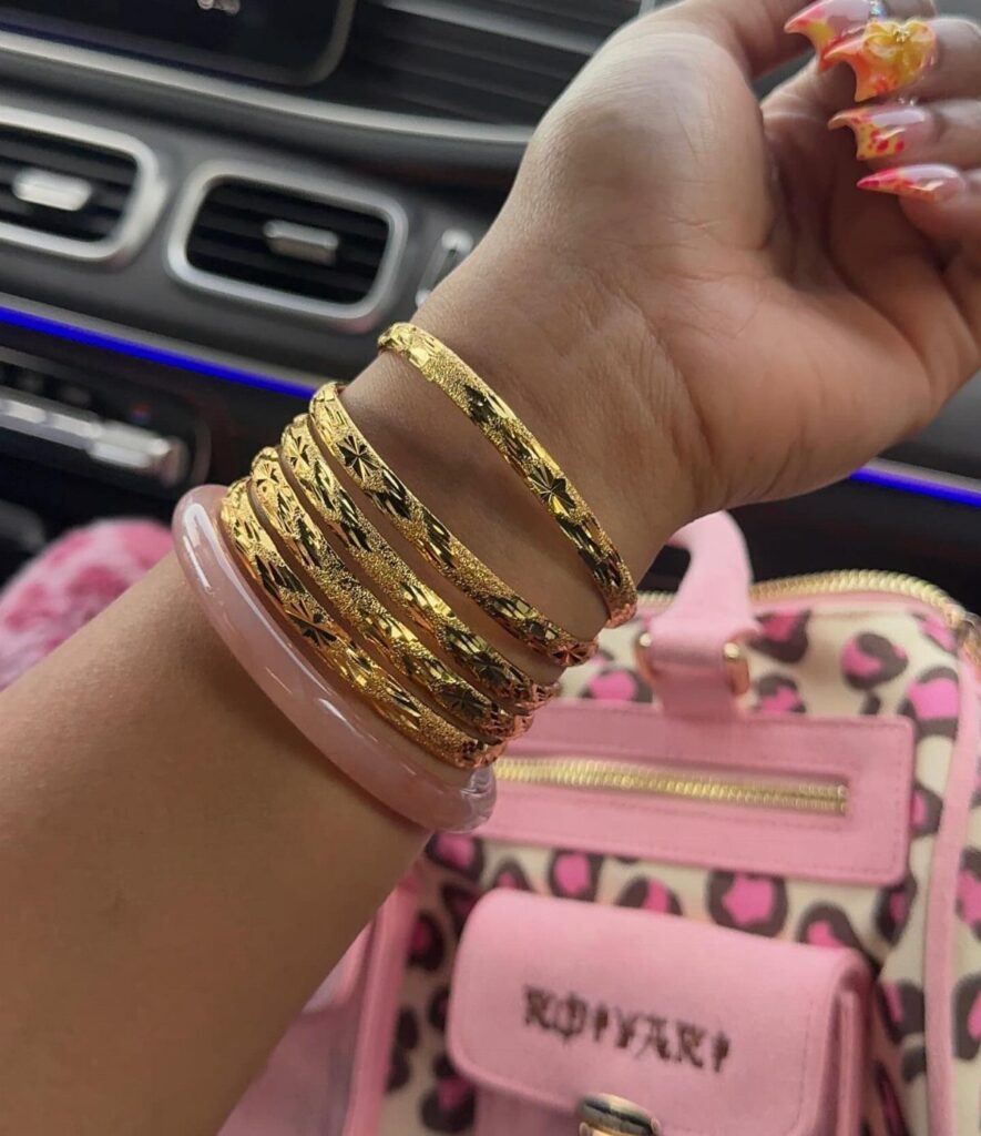 Stack of gold textured bangles and a pink bangle on a wrist