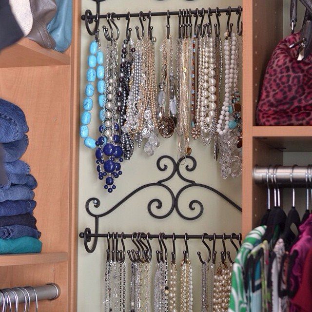 Necklaces hanging from a black metal organizer inside a wooden closet shelf.
