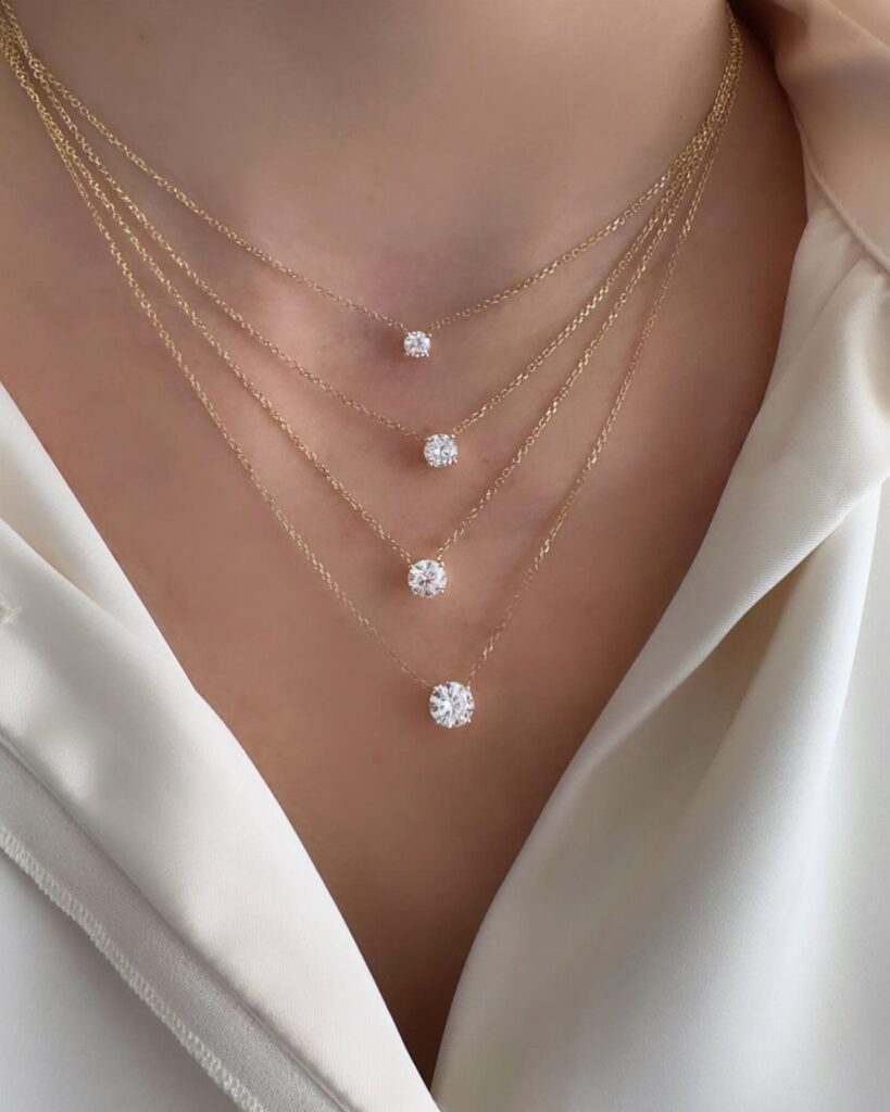 Four layered gold necklaces with round diamond pendants worn on a person's neck