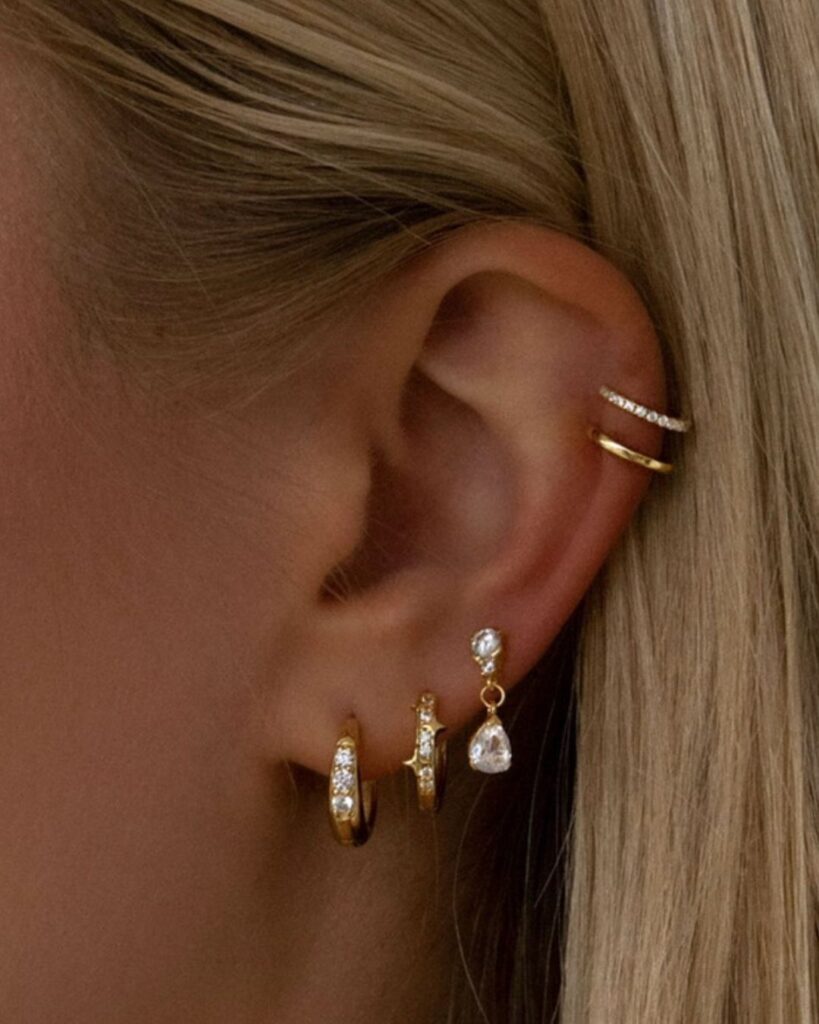 Ear with a stack of gold and diamond earrings in lobe and cartilage.