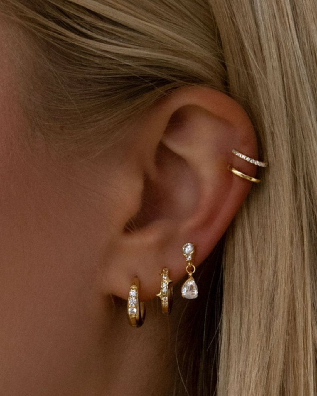 Ear with a stack of gold and diamond earrings in lobe and cartilage.