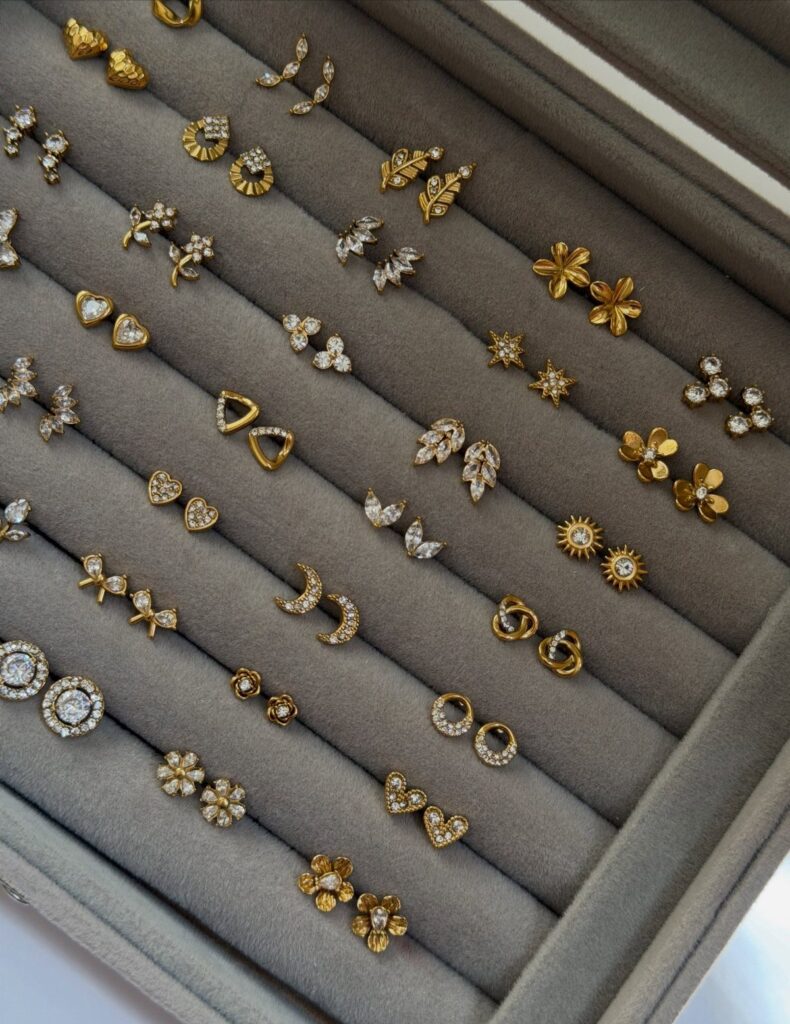 Gold and diamond stud earrings organized in a grey velvet jewelry storage box.