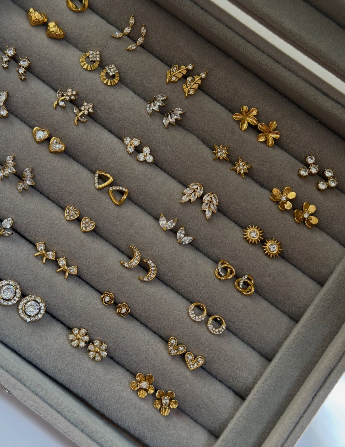 Gold and diamond stud earrings organized in a grey velvet jewelry storage box.