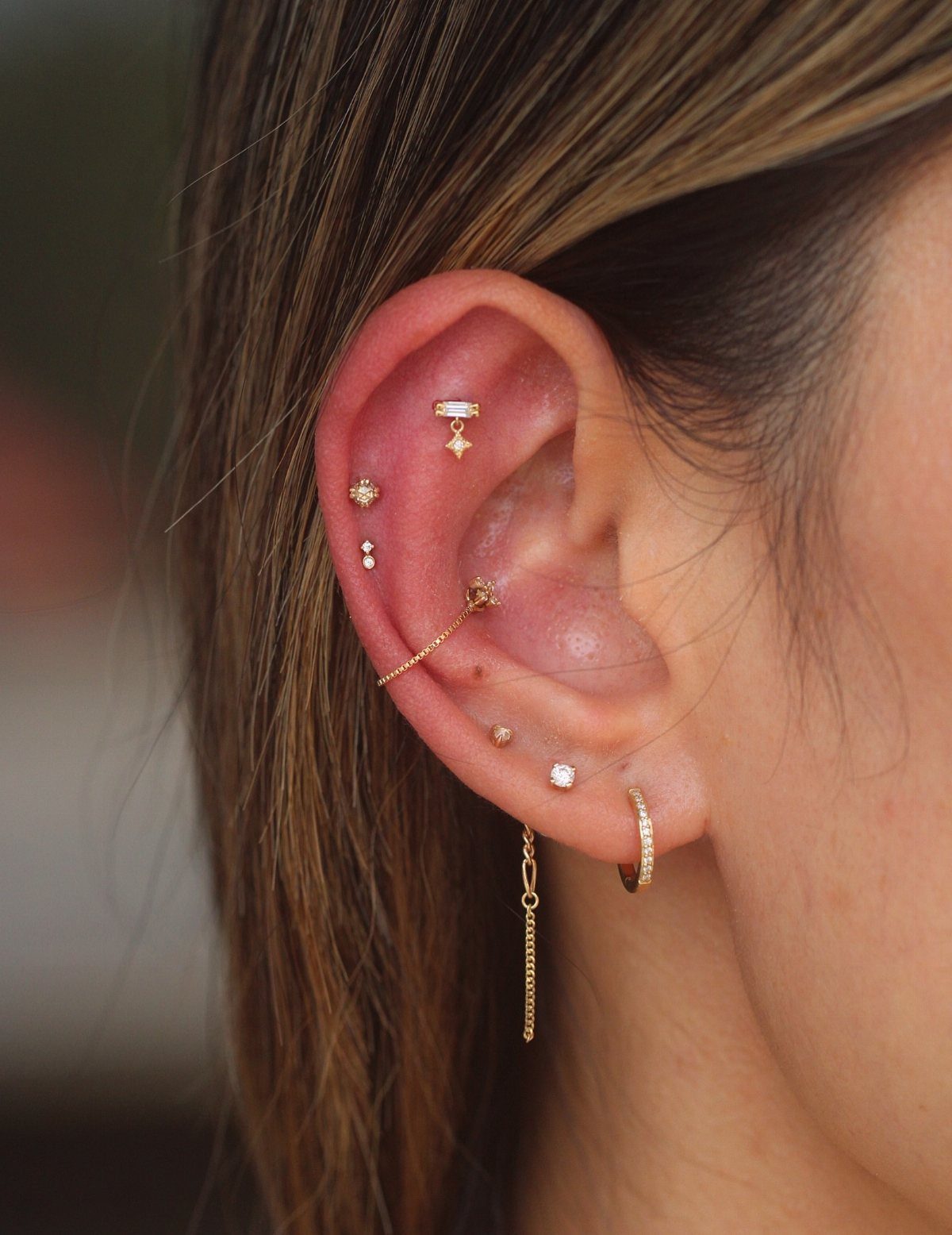 Ear with multiple gold piercings including a dangling charm at the top helix.